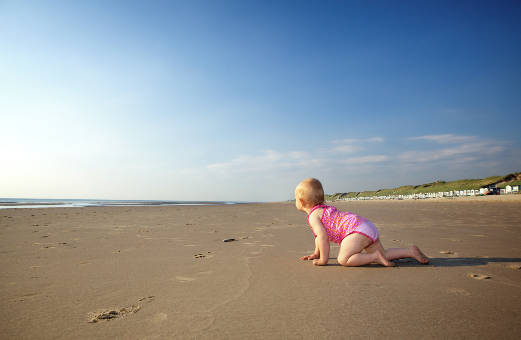 A baby crawling on a sandy beach’