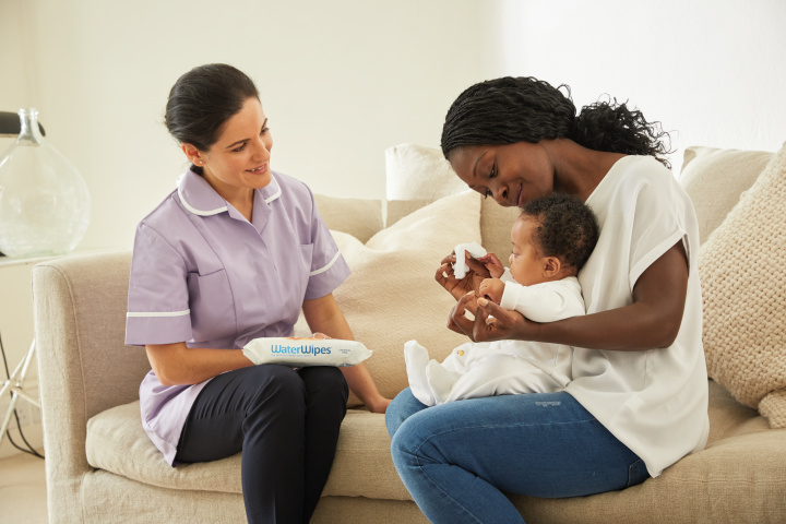 A mother cleans her baby with WaterWipes as a healthcare professional looks on