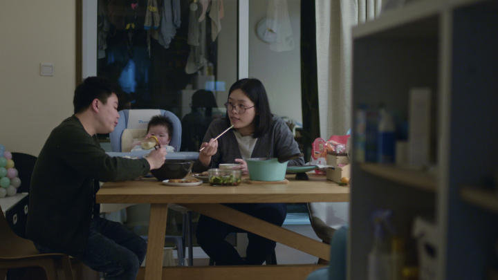 Mother and father feeding their baby at the dinner table.