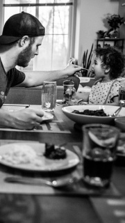 A father feeding his toddler at the dinner table.