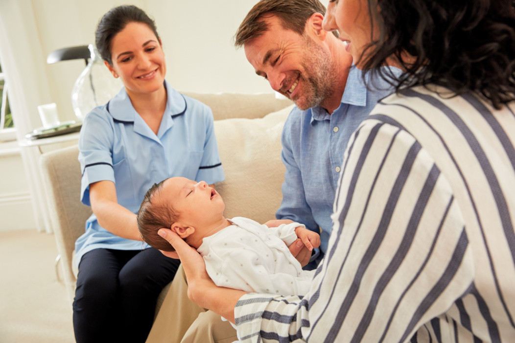 A midwife looks on as two parents hold their newborn baby