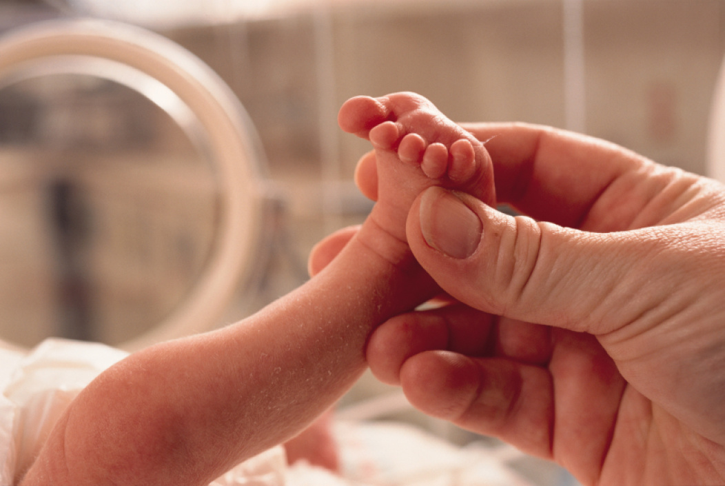 A parent holding their newborn premature baby’s foot