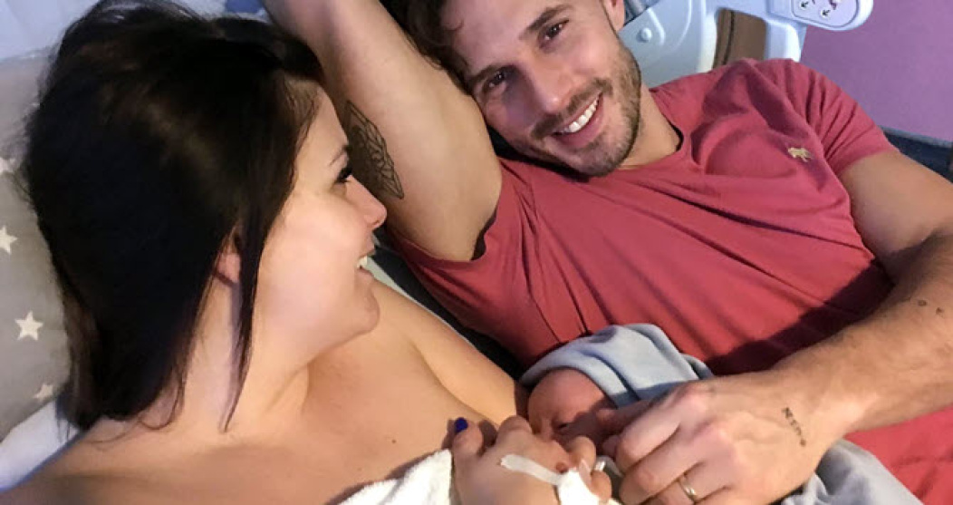 A couple on a bed with their newborn baby